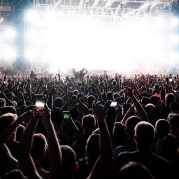 Rear view of large group of people having fun on music festival at night. Back view of excited audience with arms raised cheering in front of the stage at music concert. Copy space.